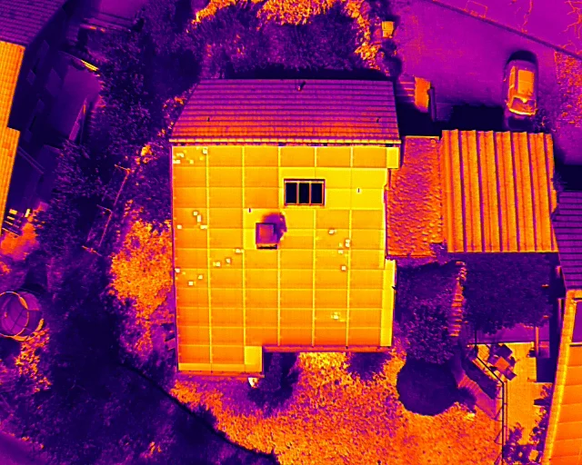 Wärmebild eines Hausdachs mit Solaranlage aus der Luft: Über die Modulfläche verteilt leuchten einzelne helle Flecken.